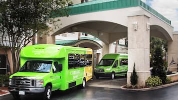 En entré till ett Courtyard Marriott-hotell med två gröna transferbussar parkerade under en viadukt med grön beväxt tak.
