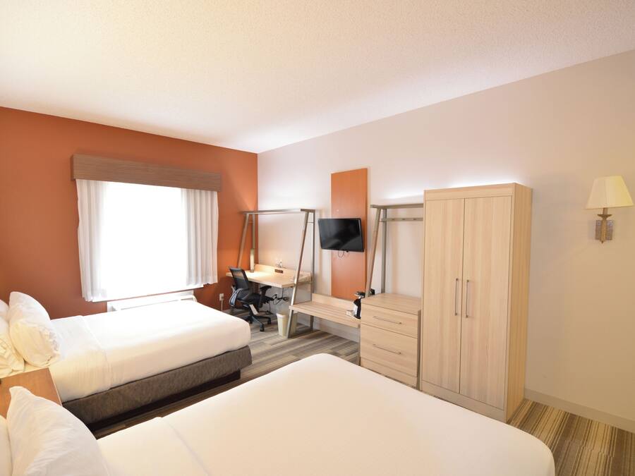 Quarto de hotel com duas camas, uma escrivaninha, uma televisão e um guarda-roupa.