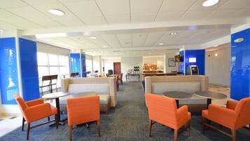 A hotel lobby with seating areas, a reception desk, and a view of the dining area.