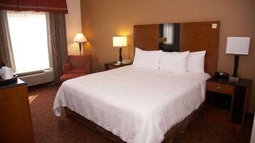 Una habitación de hotel con una cama grande, dos mesitas de noche, una silla y un escritorio.