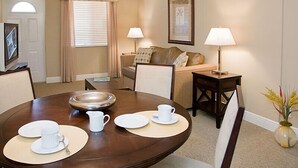 A dining area with a round table, chairs, and a buffet setup. There is a sofa and a lamp in the background. - Sun Harbour Boutique Hotel (Surfside)