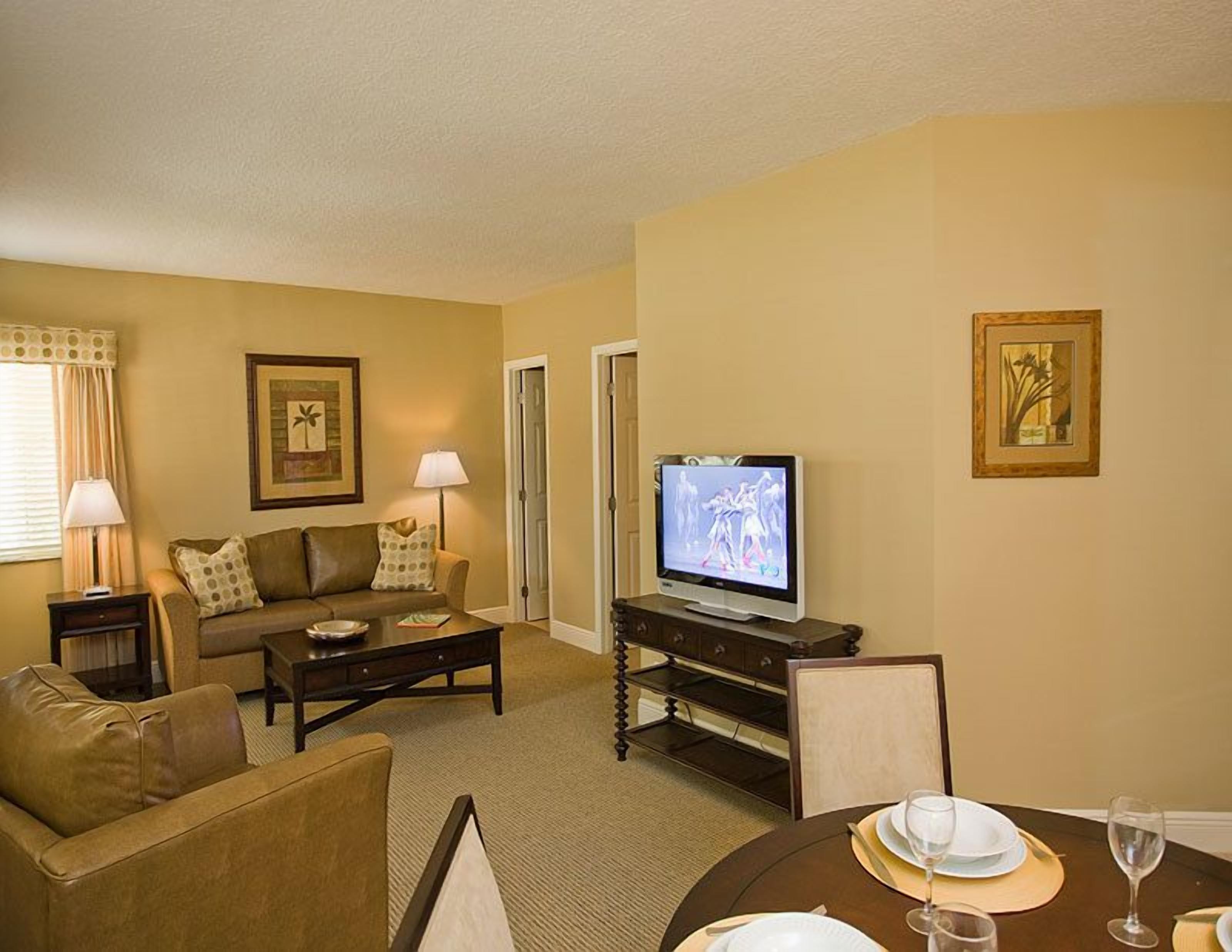 A living room with a sofa, coffee table, TV, and dining table set for two.
