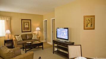 A living room with a sofa, coffee table, TV, and dining table set for two.