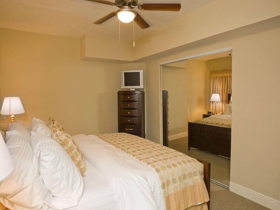 Una habitación de hotel con cama, cómoda, televisión y ventilador de techo.