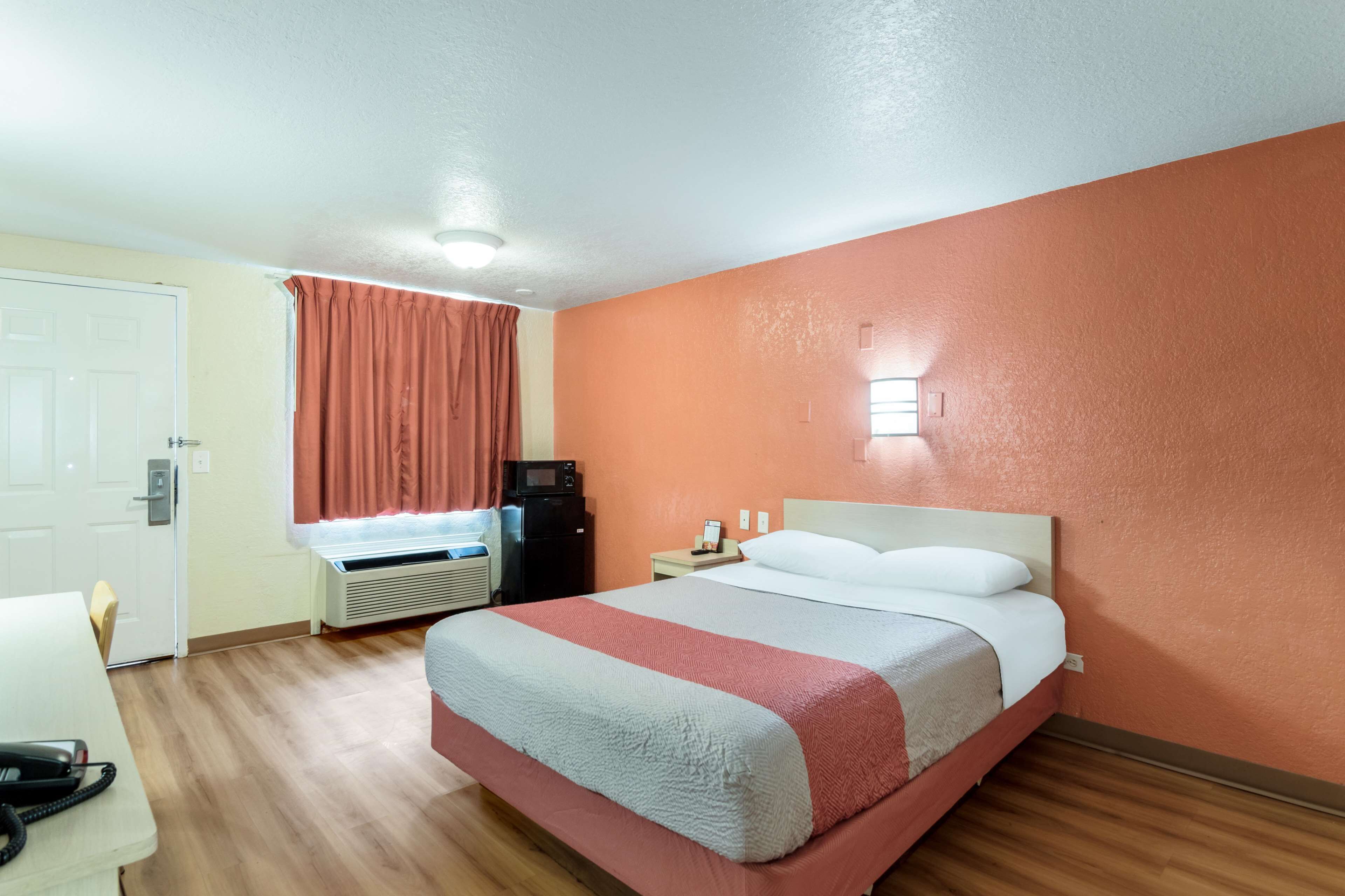 Ein Hotelzimmer mit Bett, Schreibtisch, Mikrowelle und einem fensterbepflanzten Fenster.
