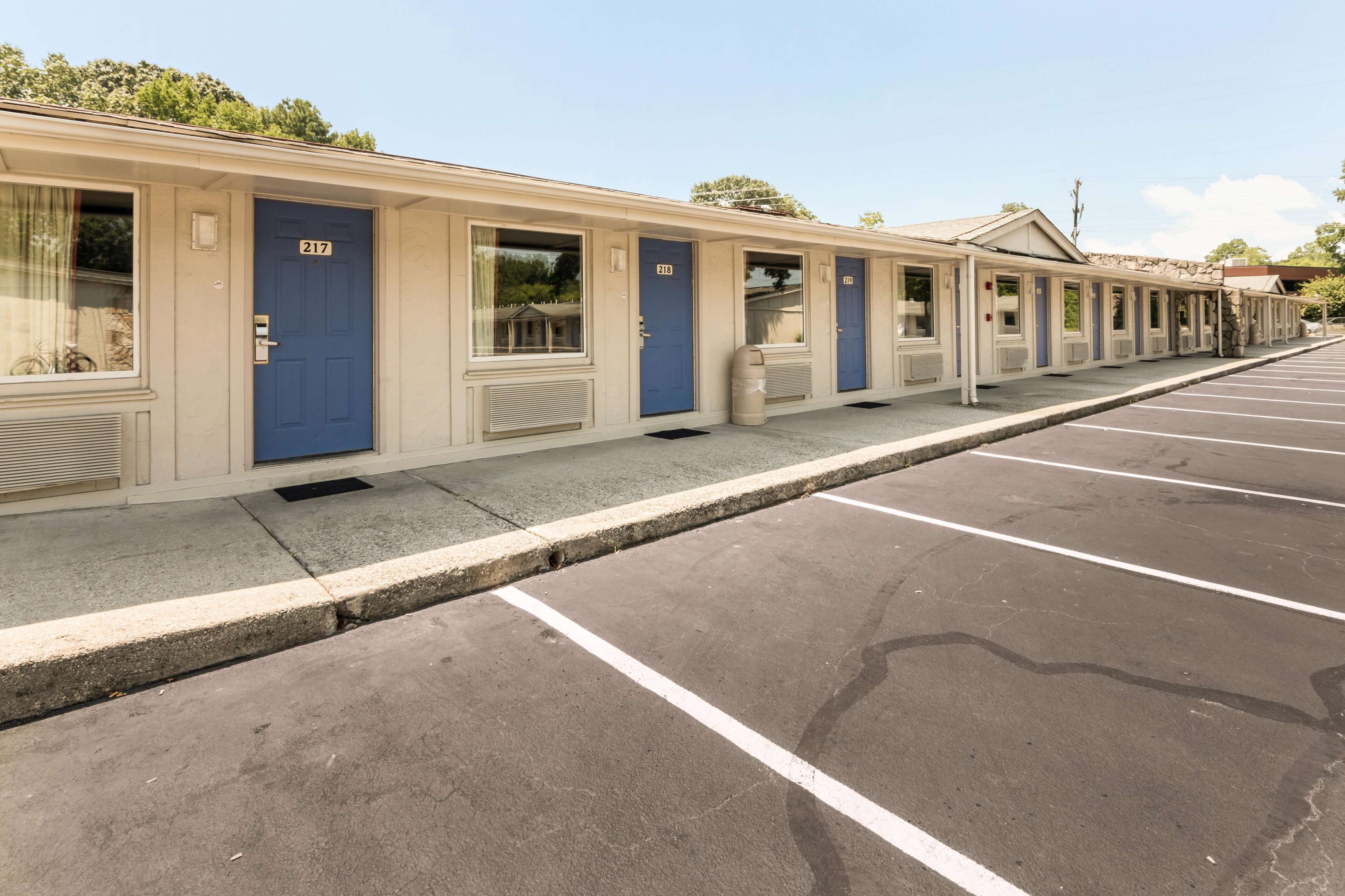 A row of motel rooms with numbered doors, a parking lot, and a clear sky.
