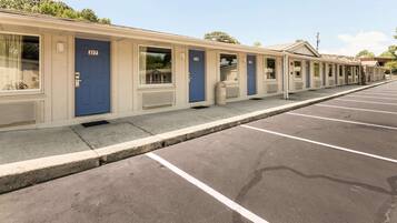 A row of motel rooms with numbered doors, a parking lot, and a clear sky.