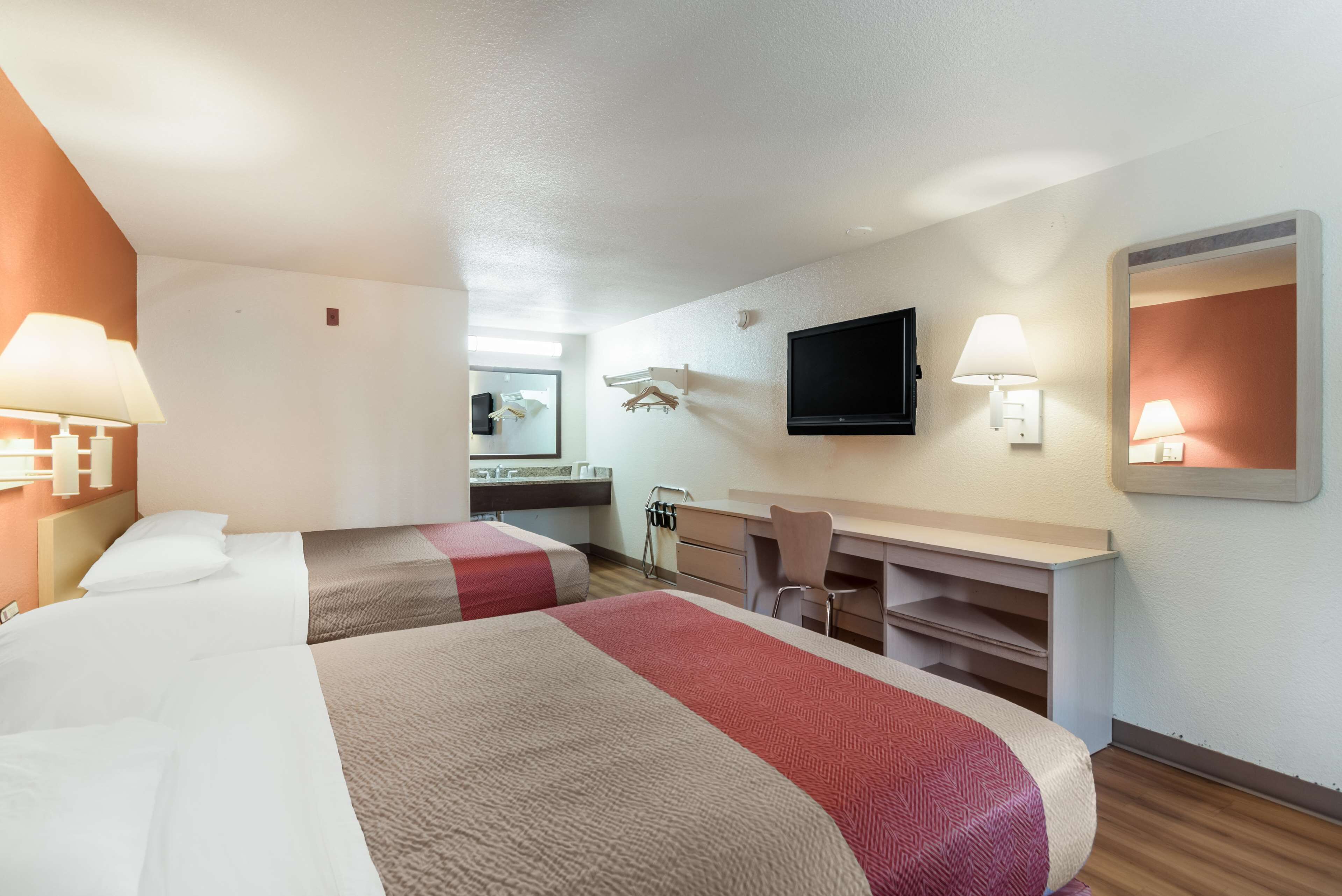 Habitación de hotel con dos camas, un escritorio, una silla, un televisor de pantalla plana y un espejo.