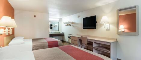 Habitación de hotel con dos camas, un escritorio, una silla, un televisor de pantalla plana y un espejo.