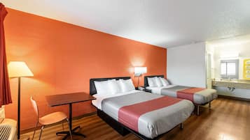 A hotel room with two beds, a desk, a chair, a lamp, and a bathroom with a mirror and sink.