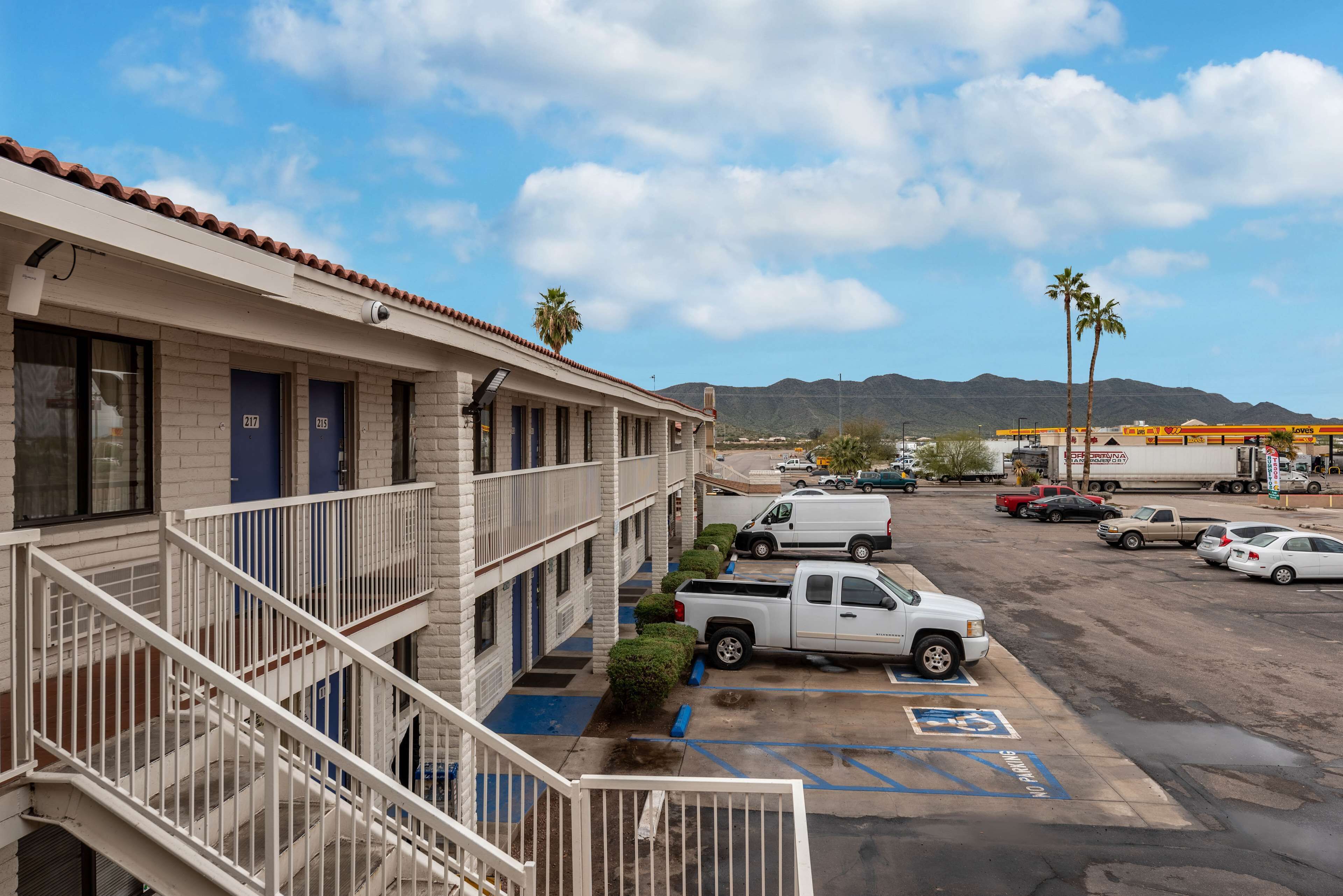A hotel with a parking lot, a white truck, and a view of mountains in the background.