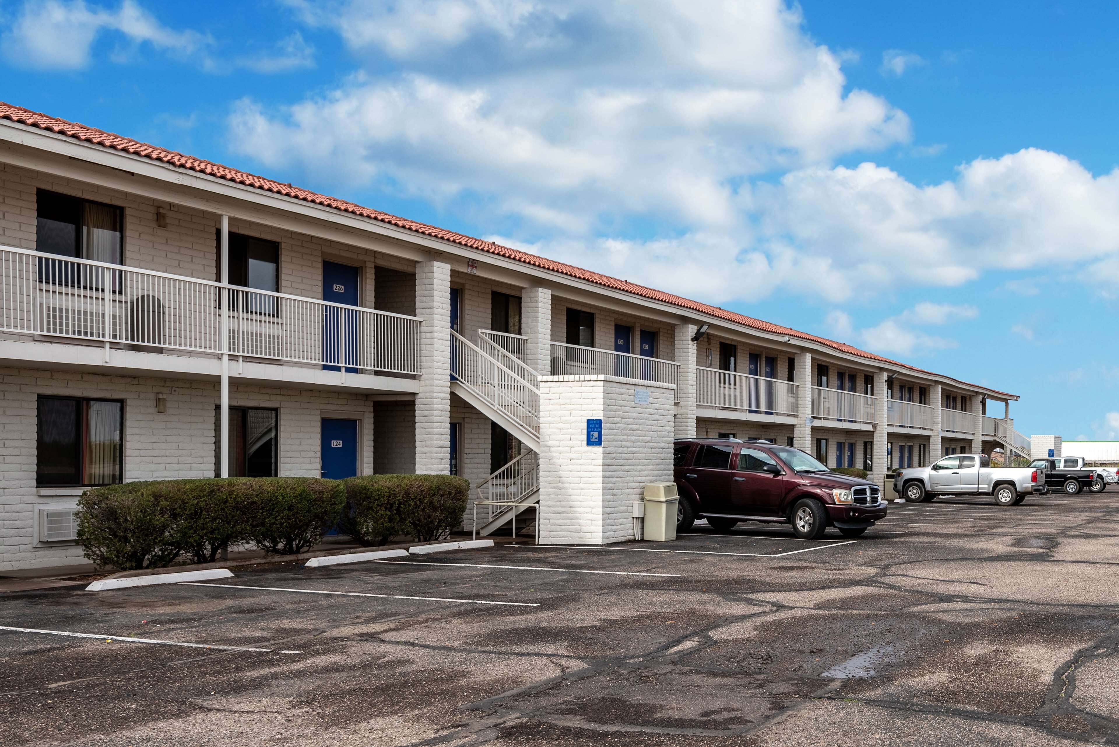 A motel with a brick facade, a covered parking area, and a staircase leading to the entrance.