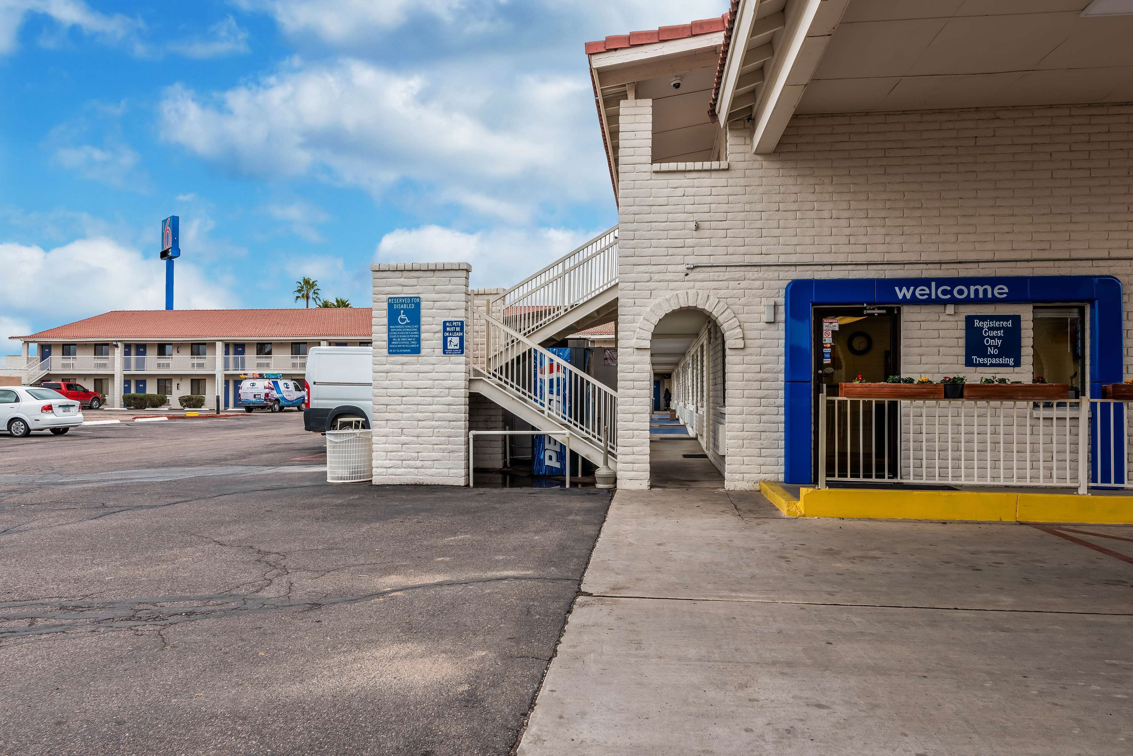 A hotel entrance with a 'welcome' sign, a wheelchair-accessible ramp, and a parking area with cars.
