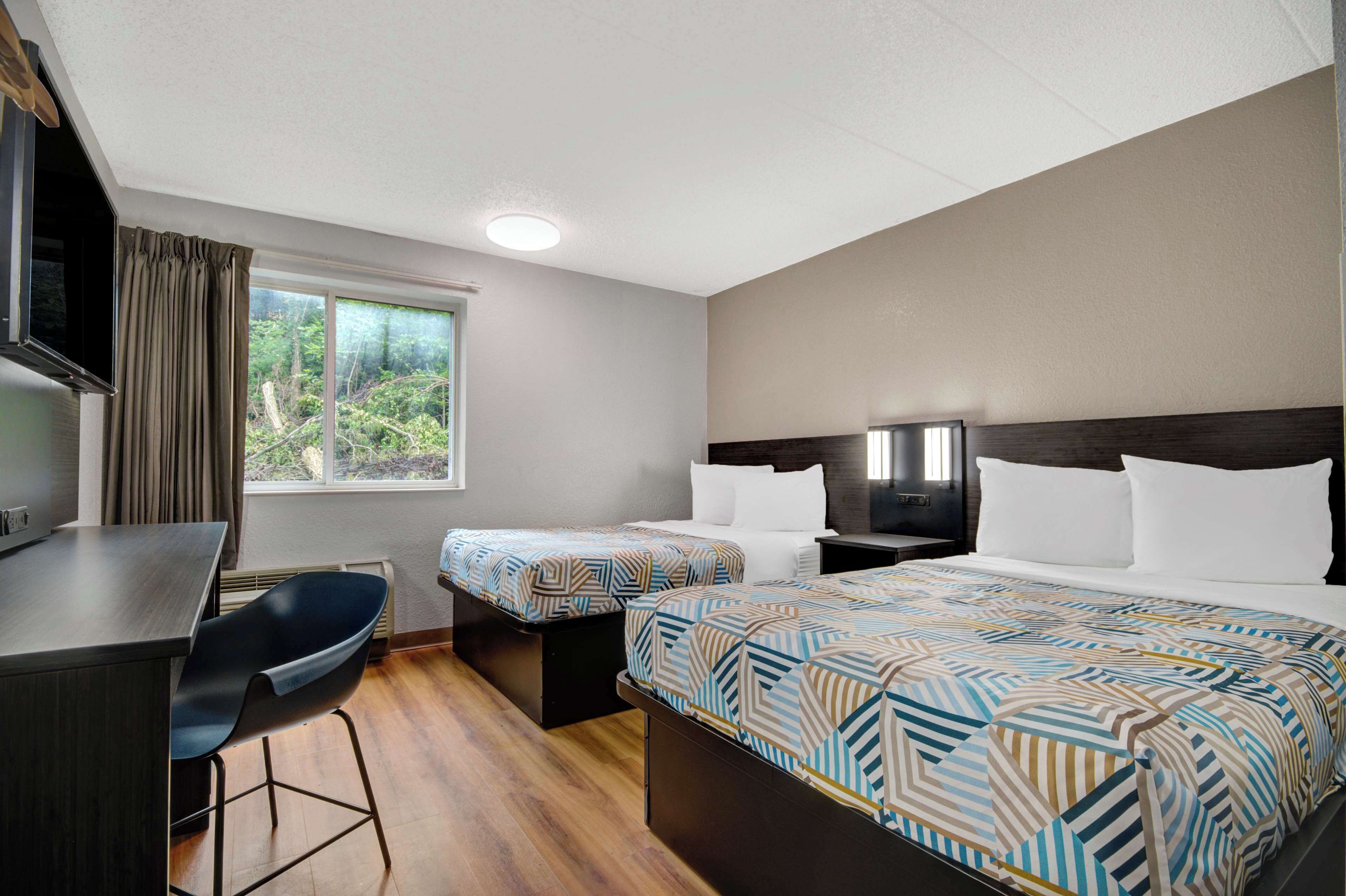 A hotel room with two beds, a desk, and a chair.