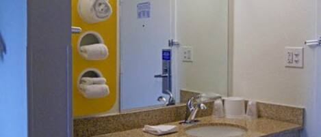 A bathroom with a granite countertop, a sink, a mirror, and a towel dispenser with multiple rolls.