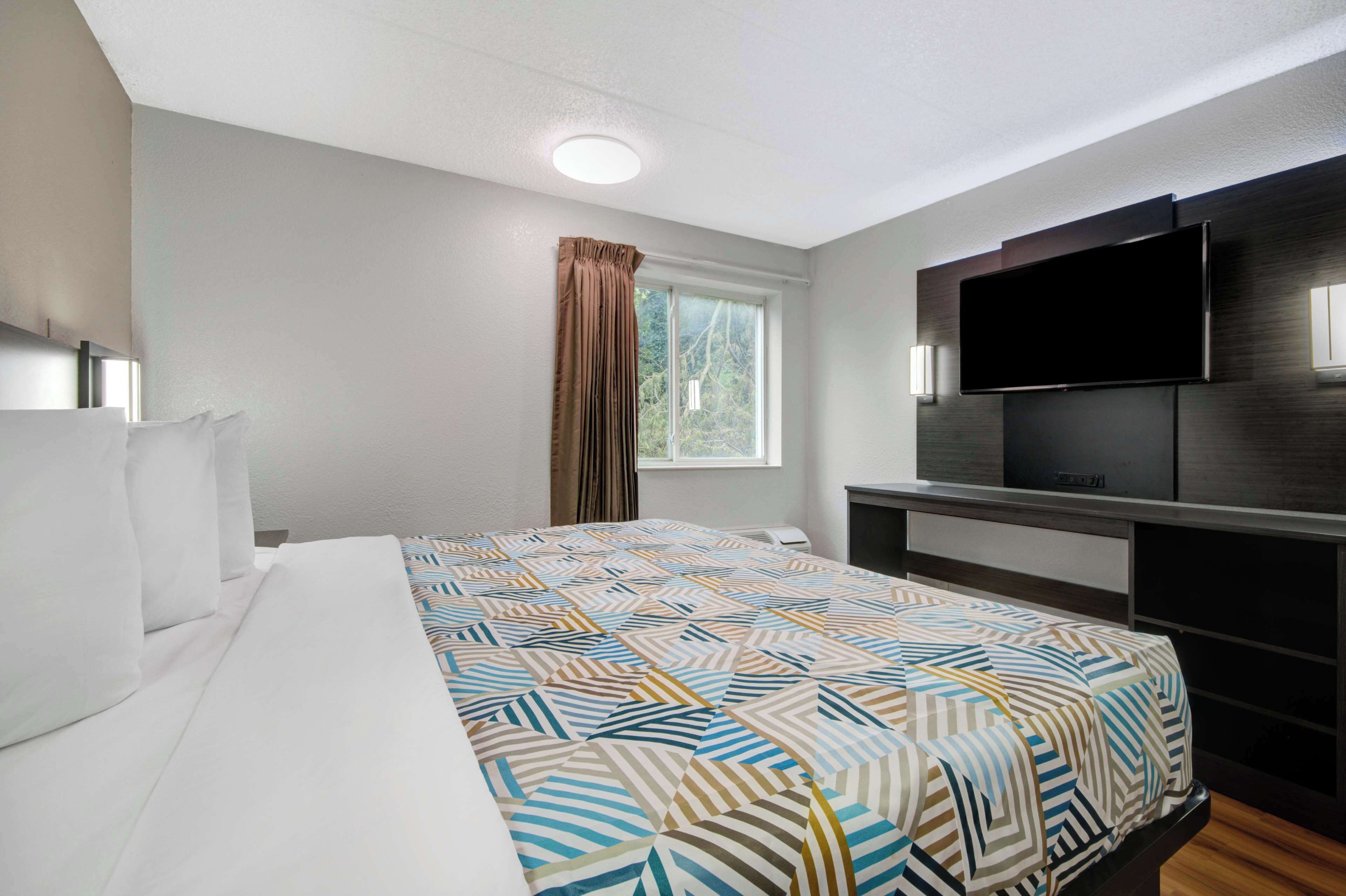 A hotel room with a large bed, a flat-screen TV mounted on the wall, a window with curtains, and a ceiling light.
