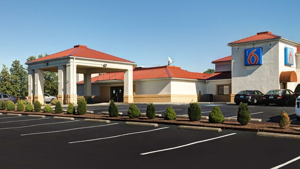 A hotel with a red roof, a covered parking area, and a sign with the number 6. - Motel 6 Shepherdsville, KY – Louisville South (Shepherdsville)