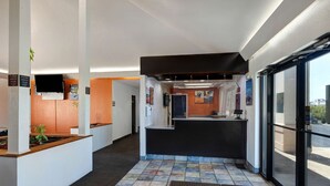 A hotel reception area with a modern design, including a reception desk, a waiting area with seating, and a view of the outside through large windows. - Motel 6 Shepherdsville, KY – Louisville South (Shepherdsville)
