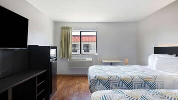 A hotel room with a TV, a desk, two beds, and a window with a view of a building.