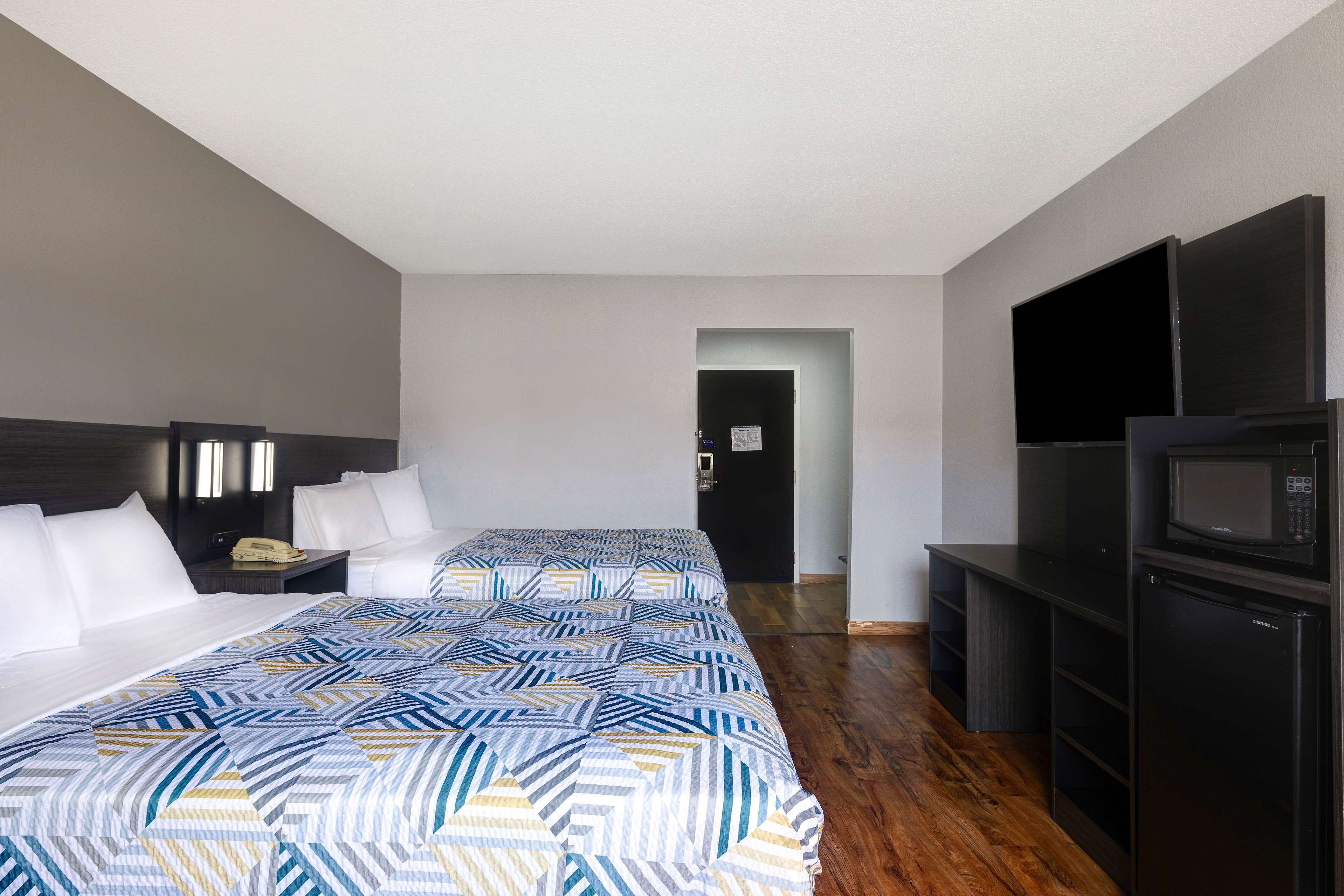 A hotel room with a large bed, a desk with a telephone, a flat-screen TV, and a microwave.