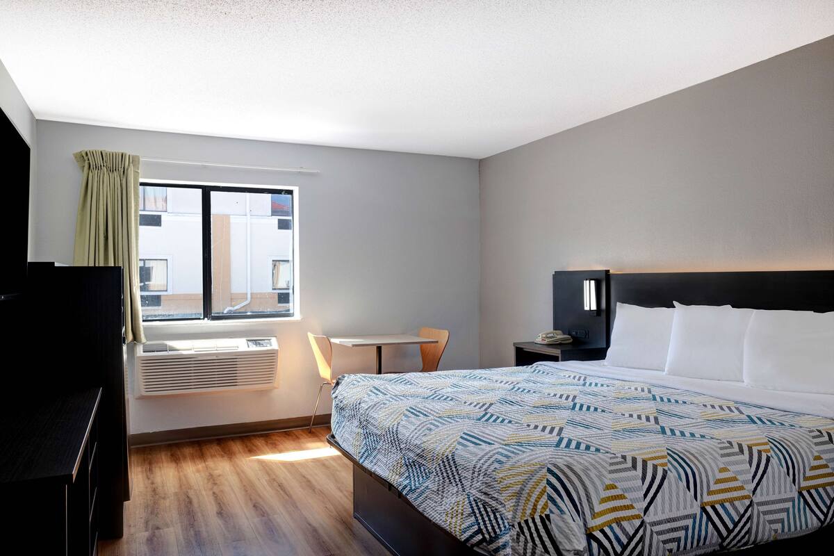 A hotel room with a large bed, a desk, a chair, and a window with curtains.