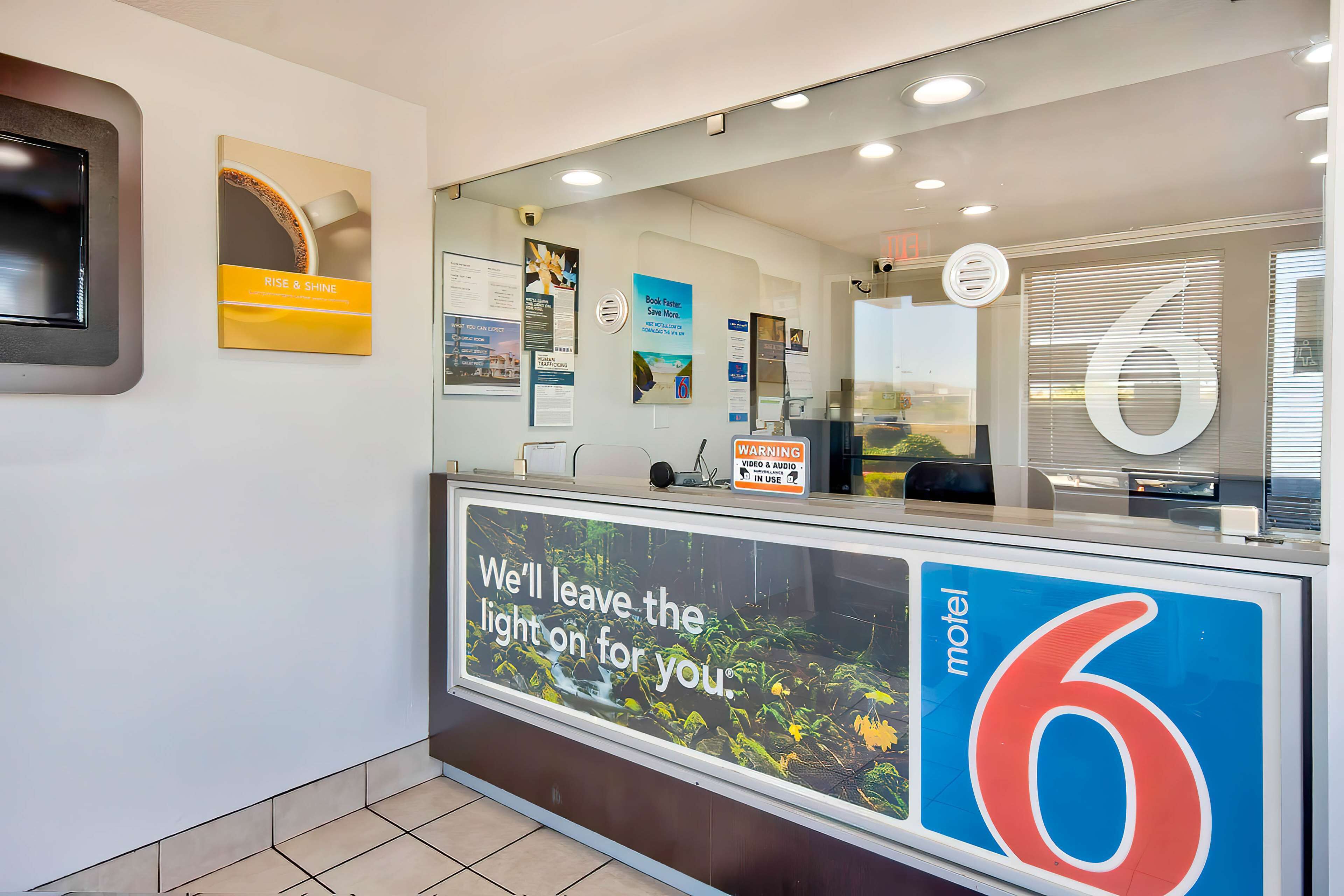 A reception desk with a large sign reading "motel 6" and a message "We'll leave the light on for you."