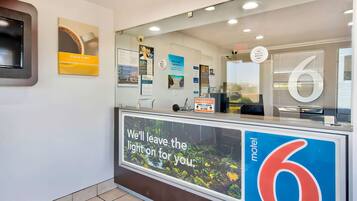 A reception desk with a large sign reading "motel 6" and a message "We'll leave the light on for you."