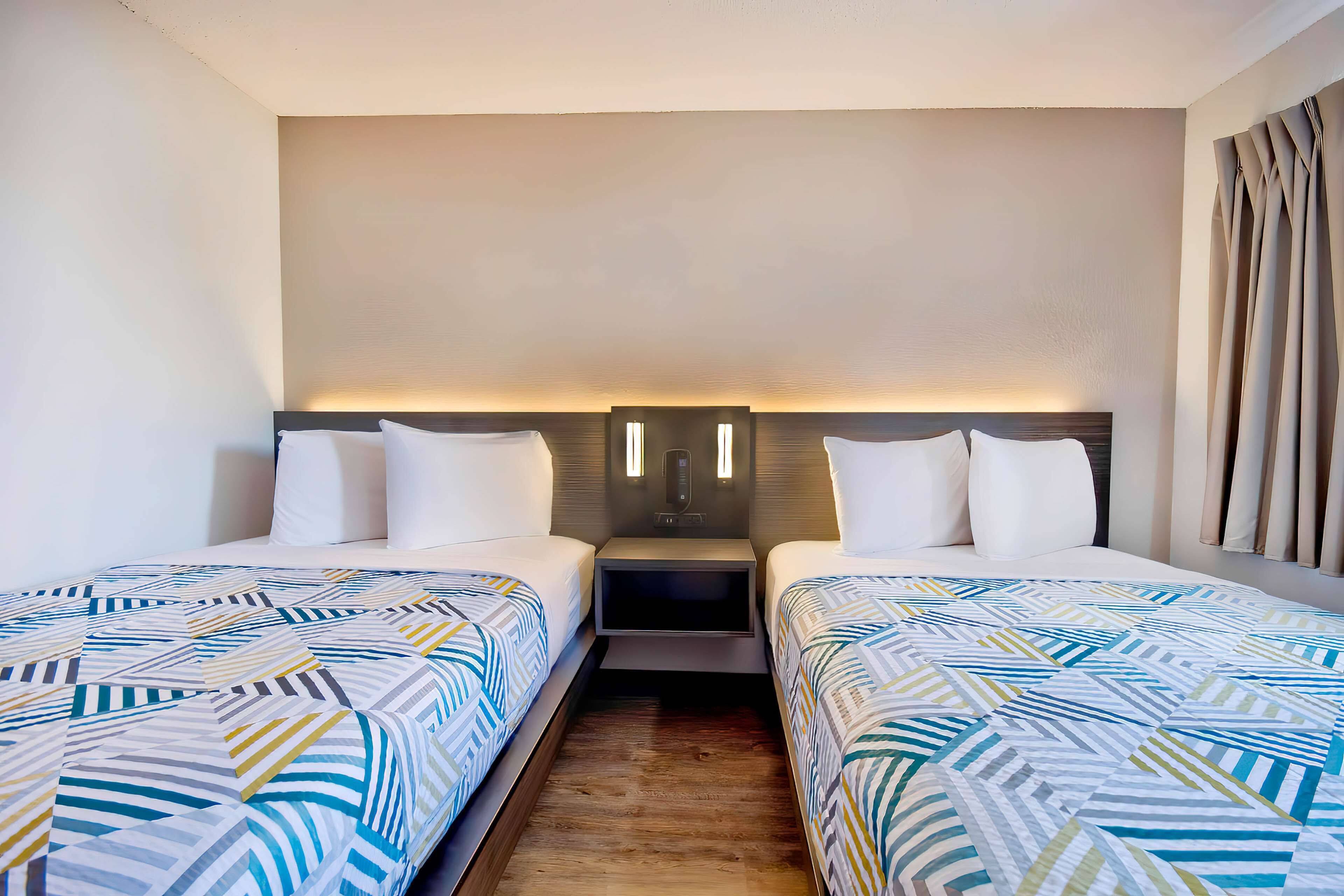 Une chambre d’hôtel avec deux lits, une table de chevet et un luminaire fixé au mur.