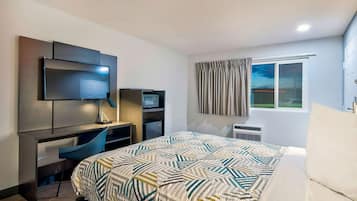 Ein Hotelzimmer mit Bett, Schreibtisch mit Computer, Fernseher und einem Fenster mit Vorhängen.