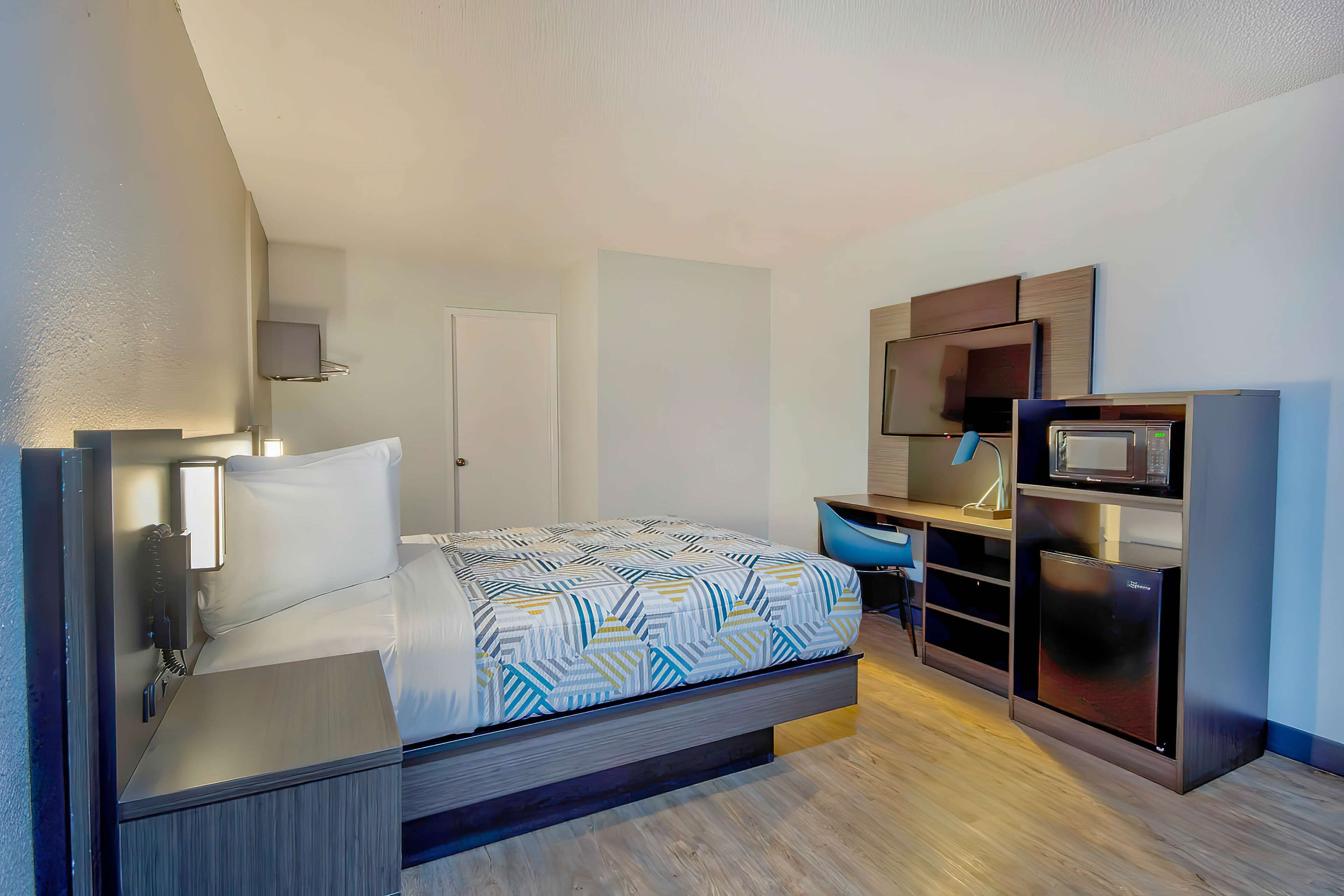 Una habitación de hotel moderna con cama, escritorio, microondas y refrigerador pequeño.