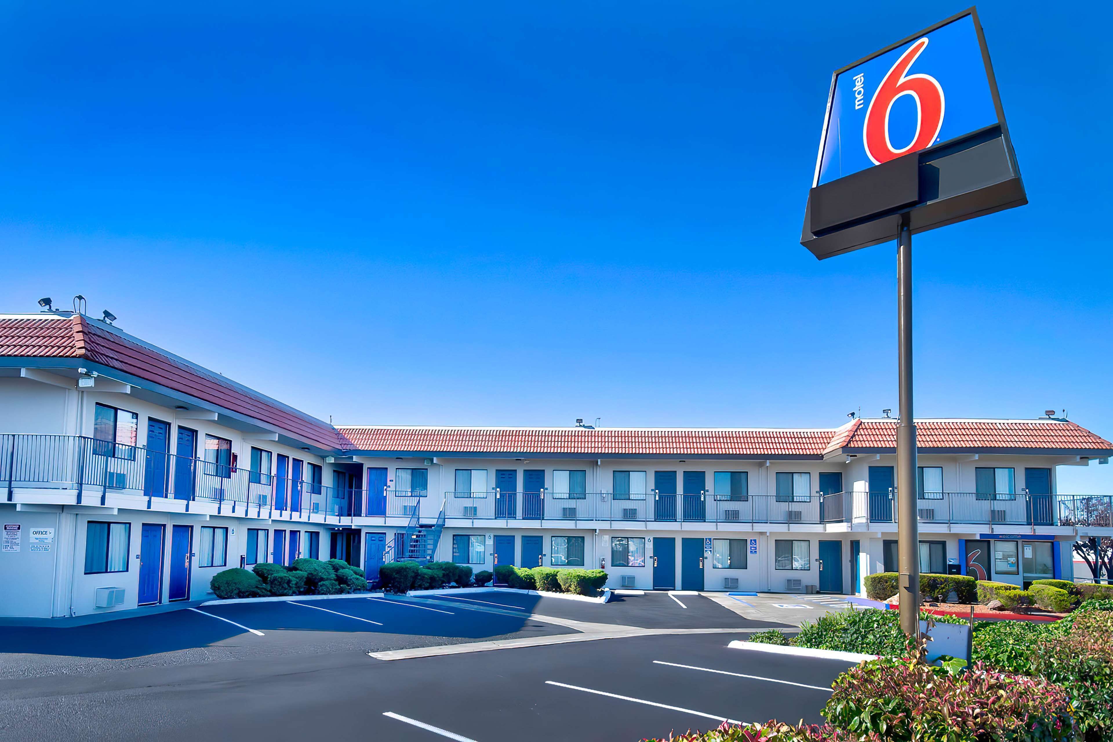 Un motel con fachada azul y blanca, un estacionamiento y un gran letrero que indica la habitación número 6.