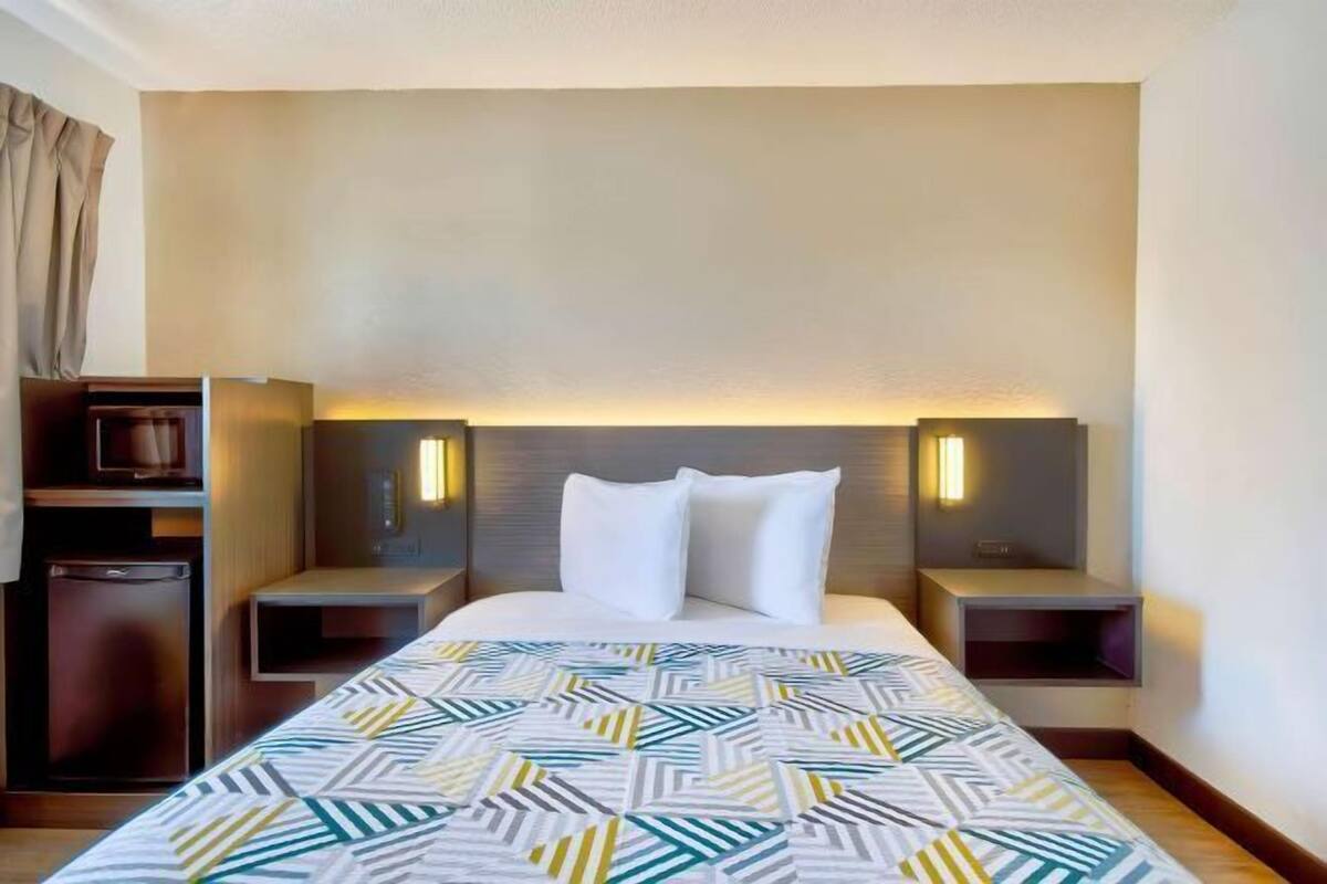 A hotel room with a bed, two bedside tables, a nightstand, a lamp, and a small cabinet.