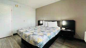 Et hotelværelse med en seng, et natbord med en lampe og en dør.