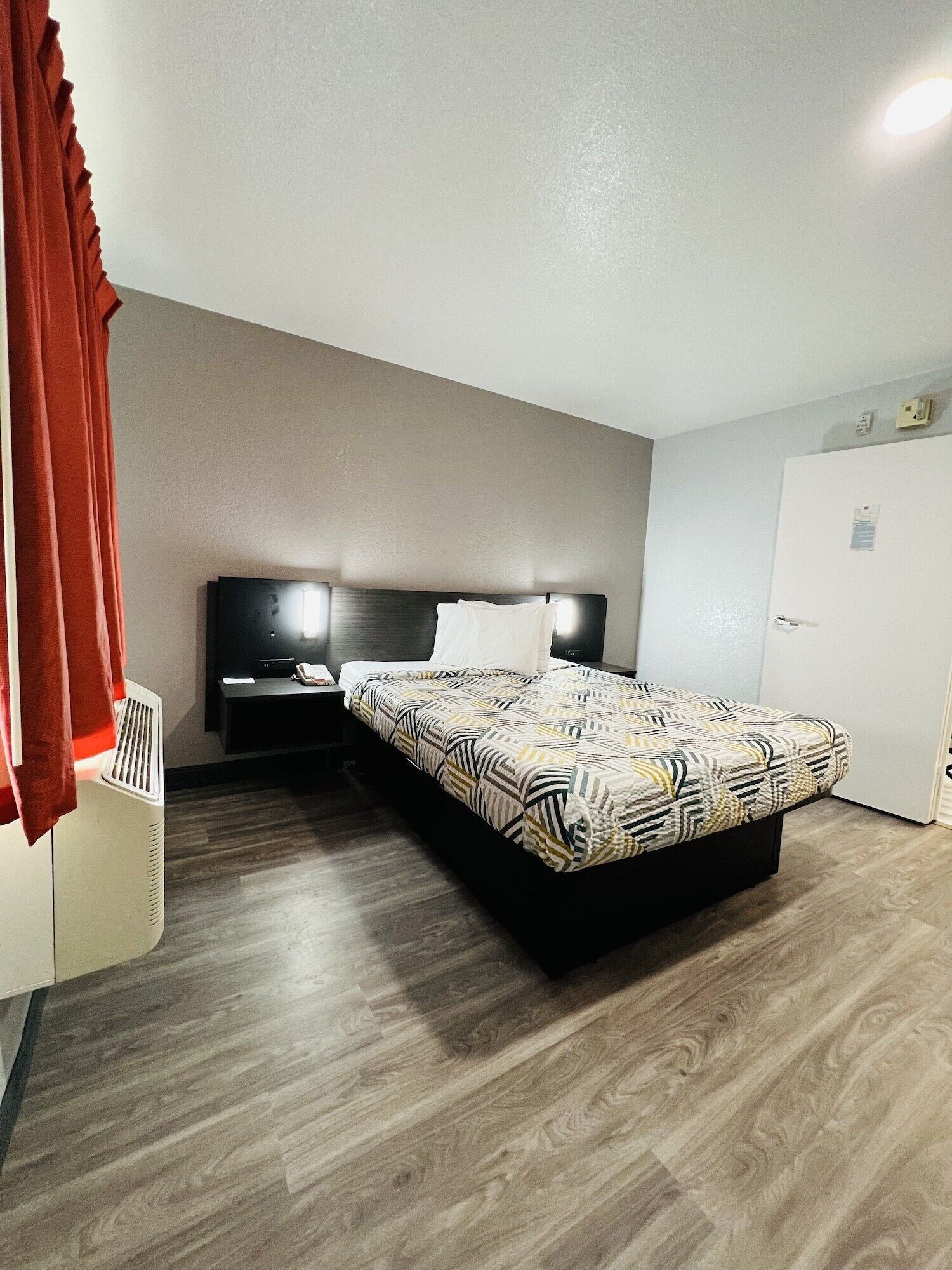 A hotel room with a bed, a bedside table, a nightstand, a heater, and a wardrobe.