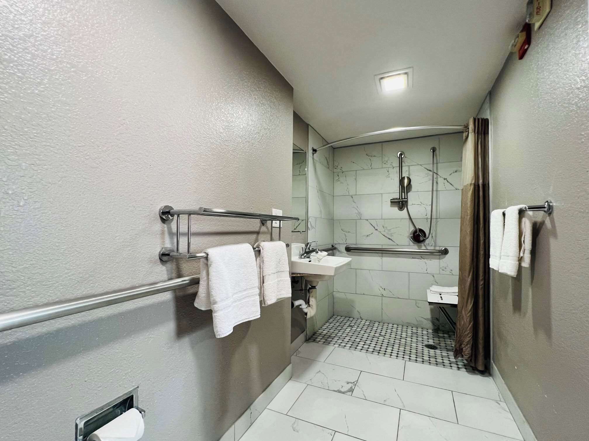 A bathroom with a shower, a sink, and a toilet. There are towels hanging on a rack.