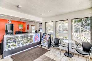 A hotel reception area with a reception desk, a clock, a digital phone, a bulletin board, and two chairs. - Motel 6 Stockton, CA - North (Stockton)