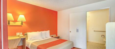 A hotel room with a bed, bedside tables, a desk, and a door leading to a bathroom.