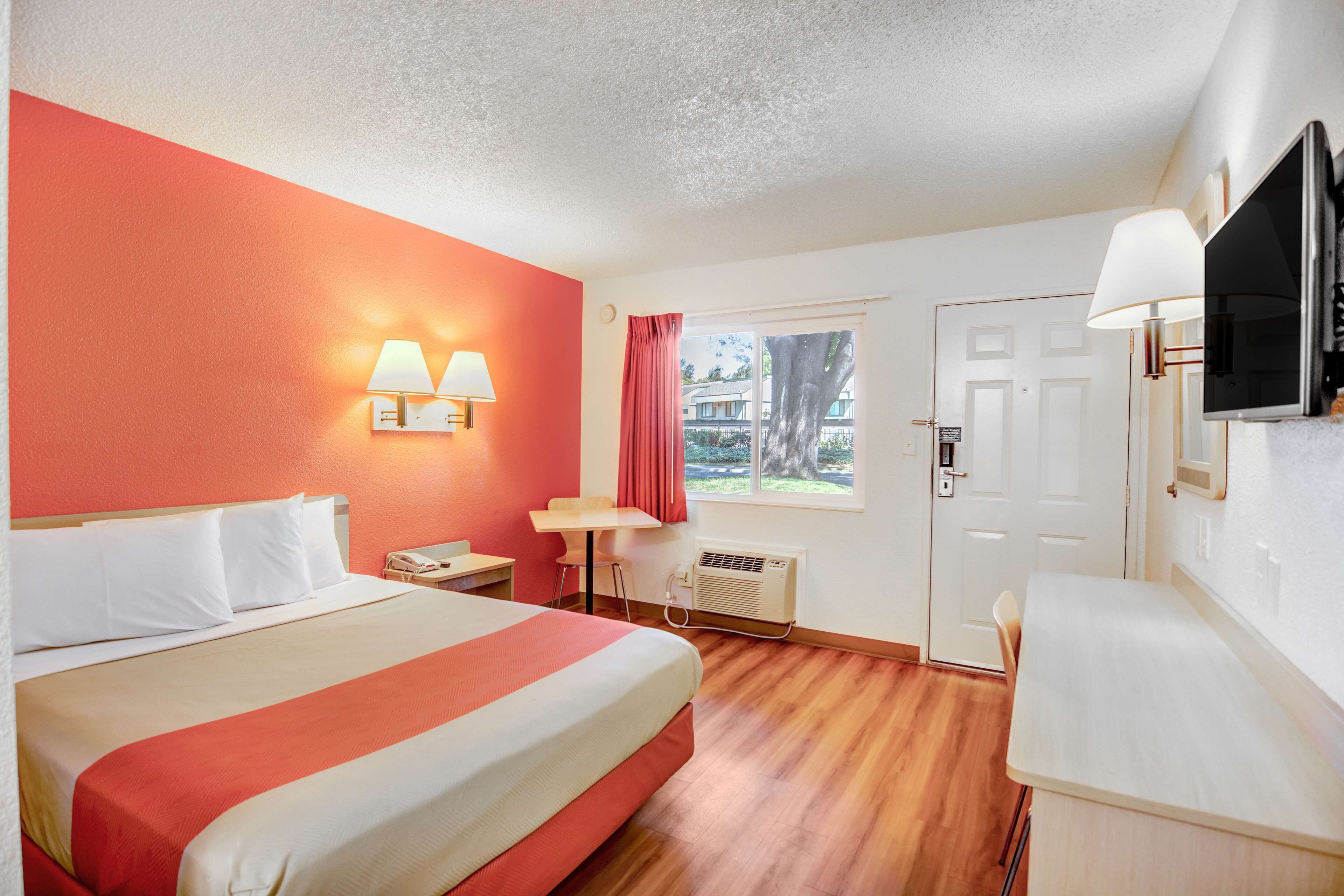 A hotel room with a bed, bedside table, lamp, and a television mounted on the wall.