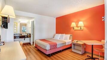 A hotel room with a bed, a desk, a chair, a small table, and a lamp.