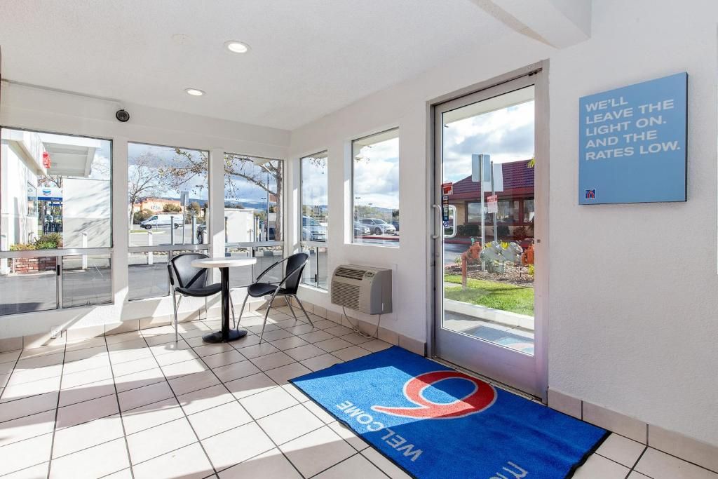 A hotel lobby with a large glass door, a blue mat with a logo, and a sign on the wall.
