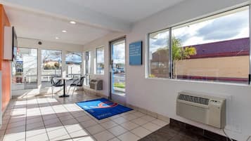 Un hall d’hôtel comprenant un comptoir d’accueil, des chaises, un tapis bleu, une grande fenêtre et un climatiseur fixé au mur.