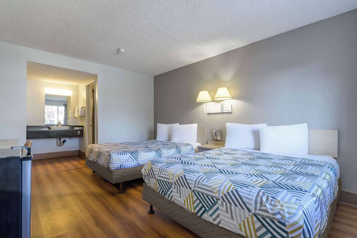 A hotel room with two beds, a desk, and a bathroom visible through an open door.