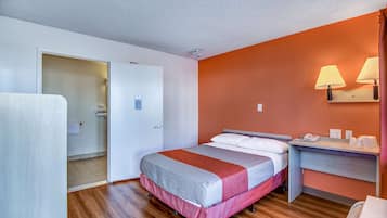 A hotel room with a bed, a desk, and a bathroom visible through an open door.
