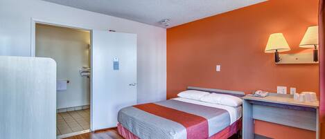 A hotel room with a bed, a desk, and a bathroom visible through an open door.