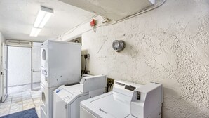 A laundry room with multiple washing machines and dryers, a control panel, and a door leading to another room. - Motel 6 Everett, WA - South (Everett)