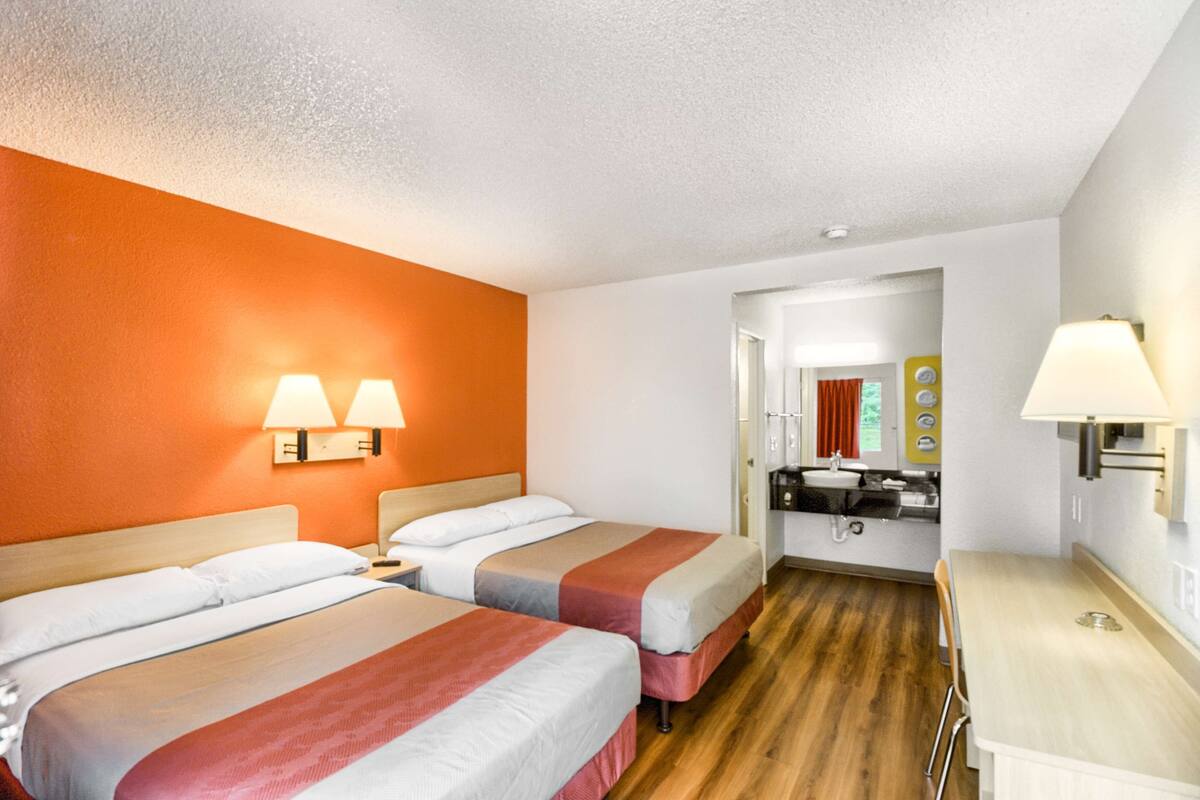 A hotel room with two beds, a kitchenette, and a bathroom visible through an open door.