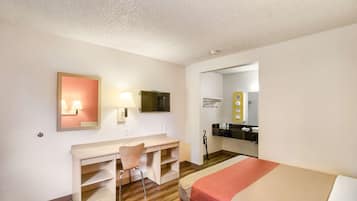 A hotel room with a bed, a desk with a chair, a TV, and a mirror.