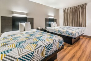 A hotel room with two beds, each with a patterned bedspread, bedside tables with lamps, and a wooden floor. - Motel 6 Irving, TX - Dallas (Irving)