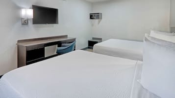 Habitación de hotel con dos camas, un escritorio con silla, un televisor montado en la pared y un perchero.