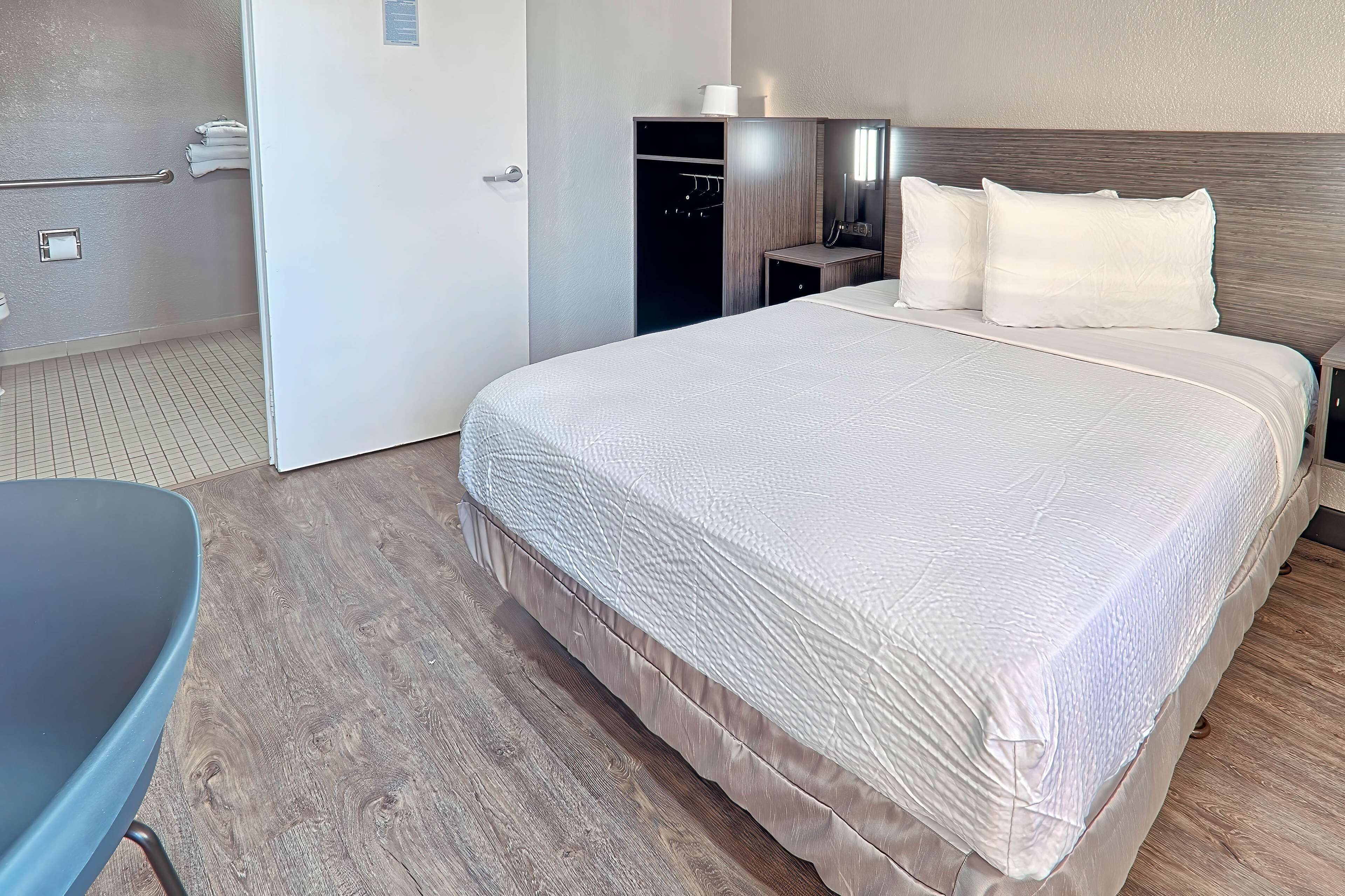 A hotel room with a large bed, a bedside table, a chair, a wardrobe, and a bathroom with a towel rack.